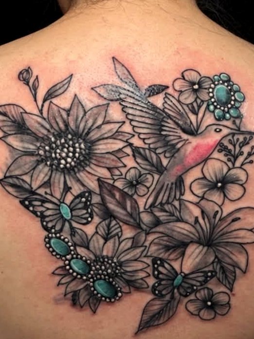 Black-and-grey back piece - a hummingbird among sunflowers and lilies, picked out with turquoise stones.