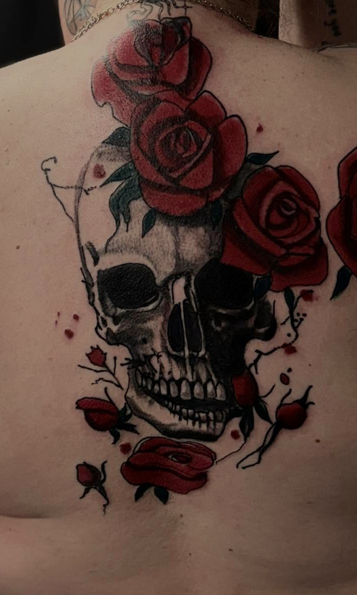Black-and-grey skull wrapped in bold red roses, upper back.